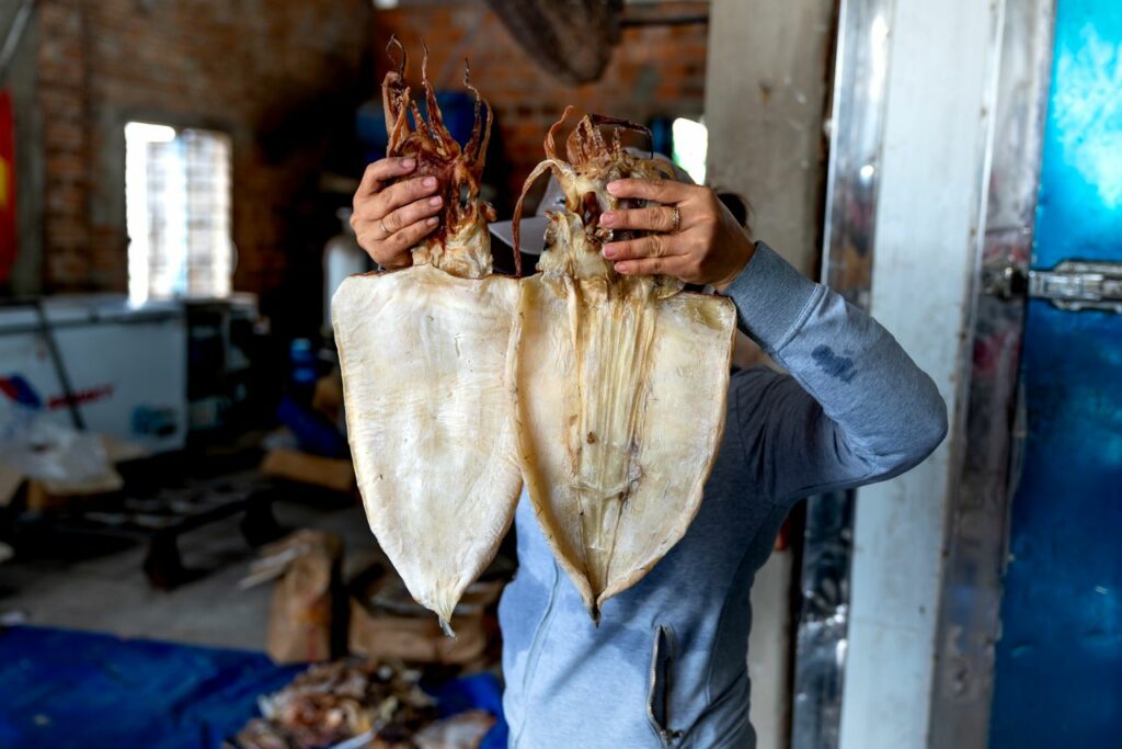 A person holds two large dried squids in an indoor warehouse environment, showcasing seafood preparation.