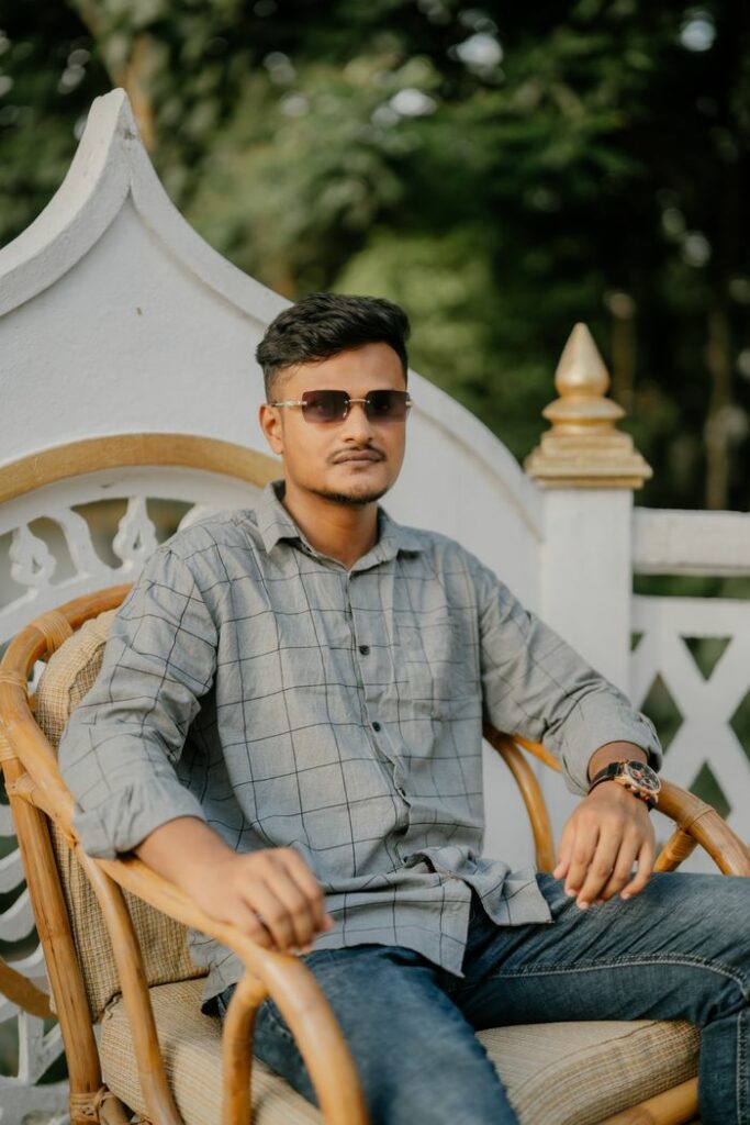 Casually dressed man wearing sunglasses sitting on a wicker chair outdoors.